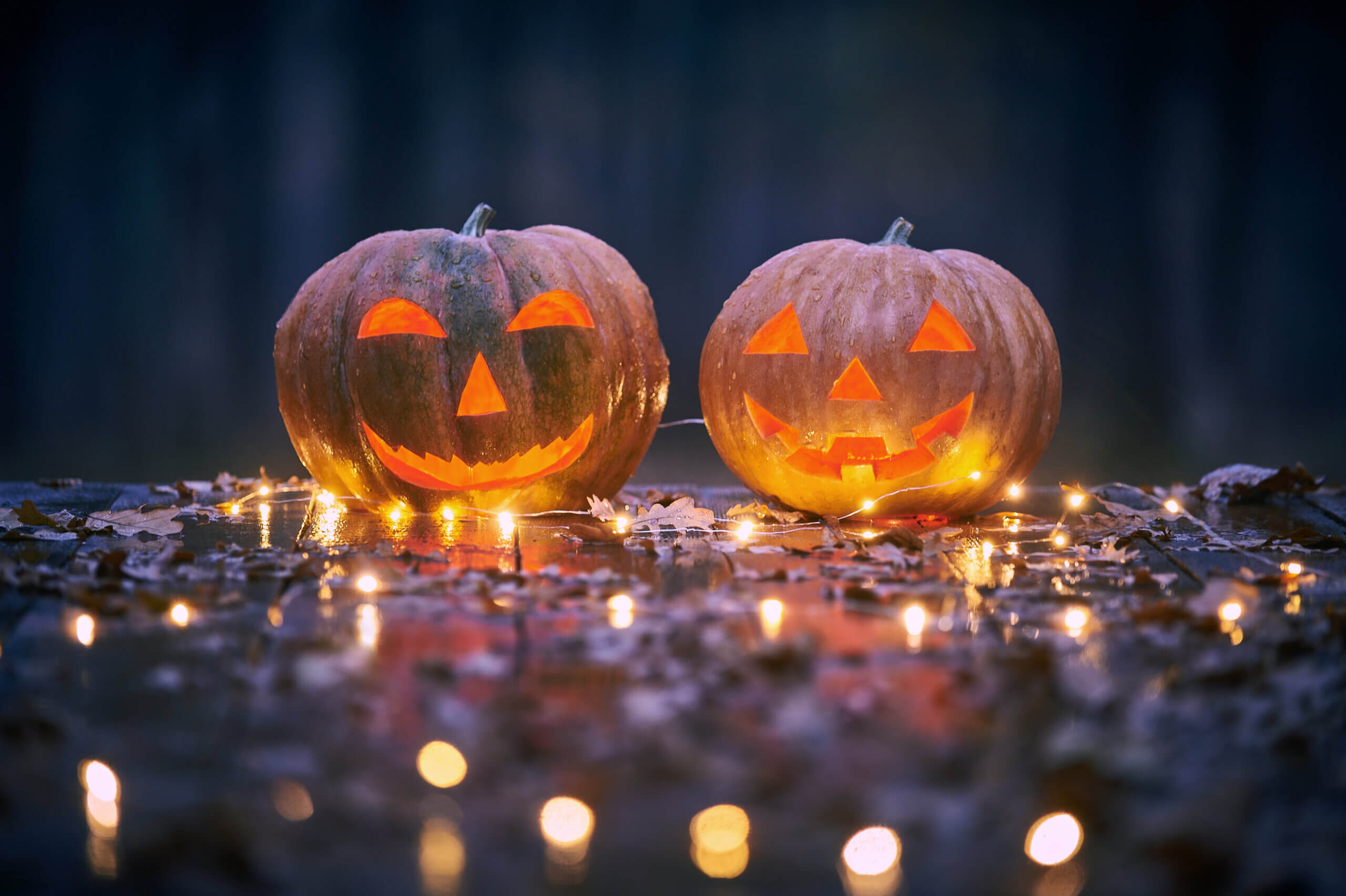 Two smiling Halloween Pumpkins on a wooden table with lights In A Mystic Forest At Night